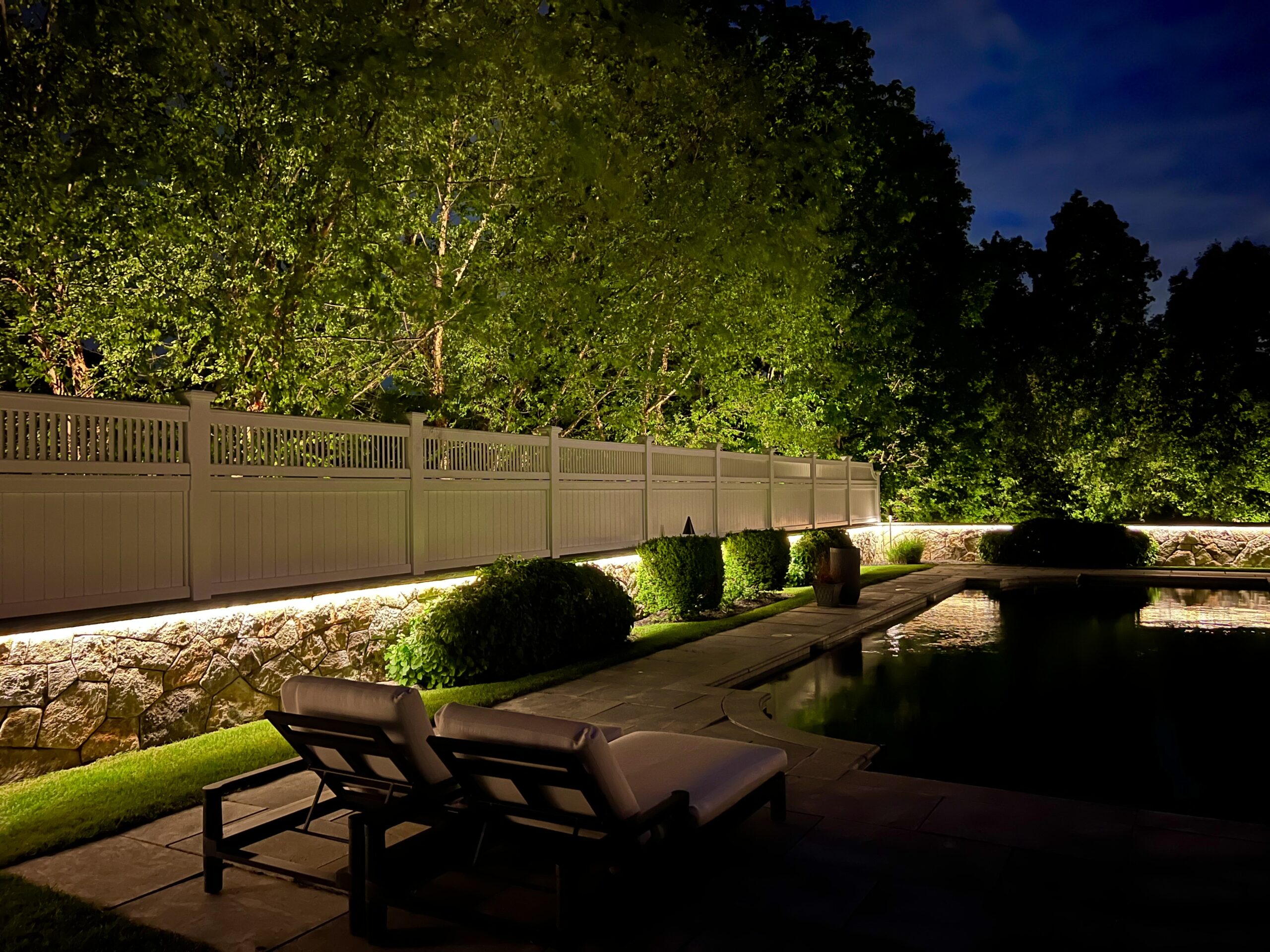 Professional outdoor lighting design illuminating a backyard patio and garden wall at night — NightView Outdoor Lighting Massachusetts