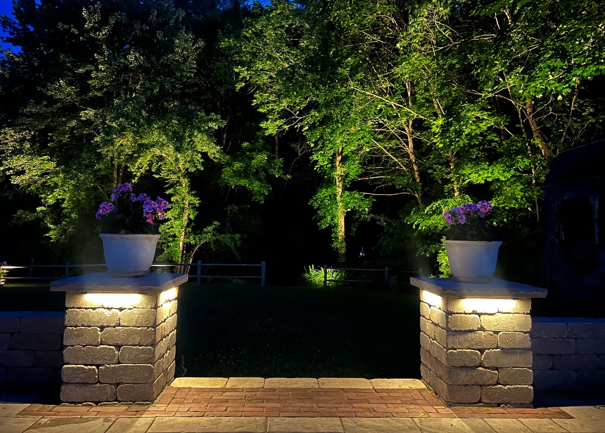 Specialty backyard lighting installation by NightView Outdoor Lighting accenting stone pillars and garden plantings with warm architectural uplighting