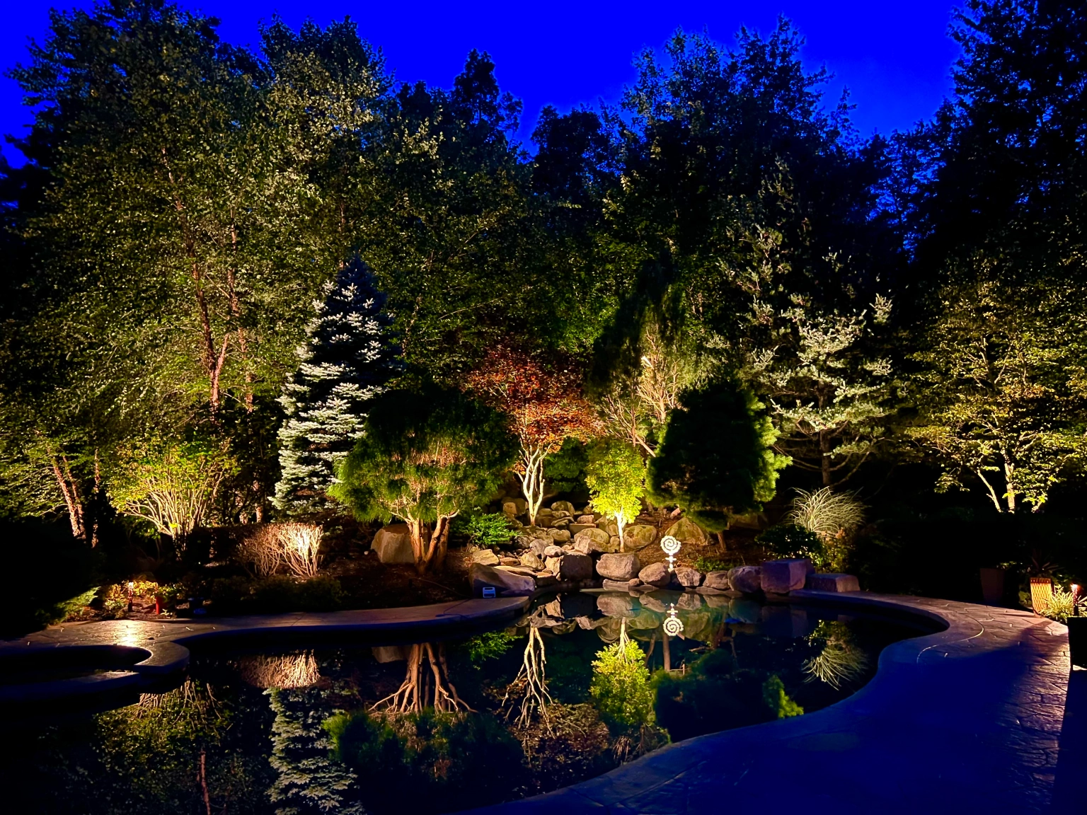 Landscape lighting design highlighting trees, garden, and pool reflection at night — NightView Outdoor Lighting Massachusetts